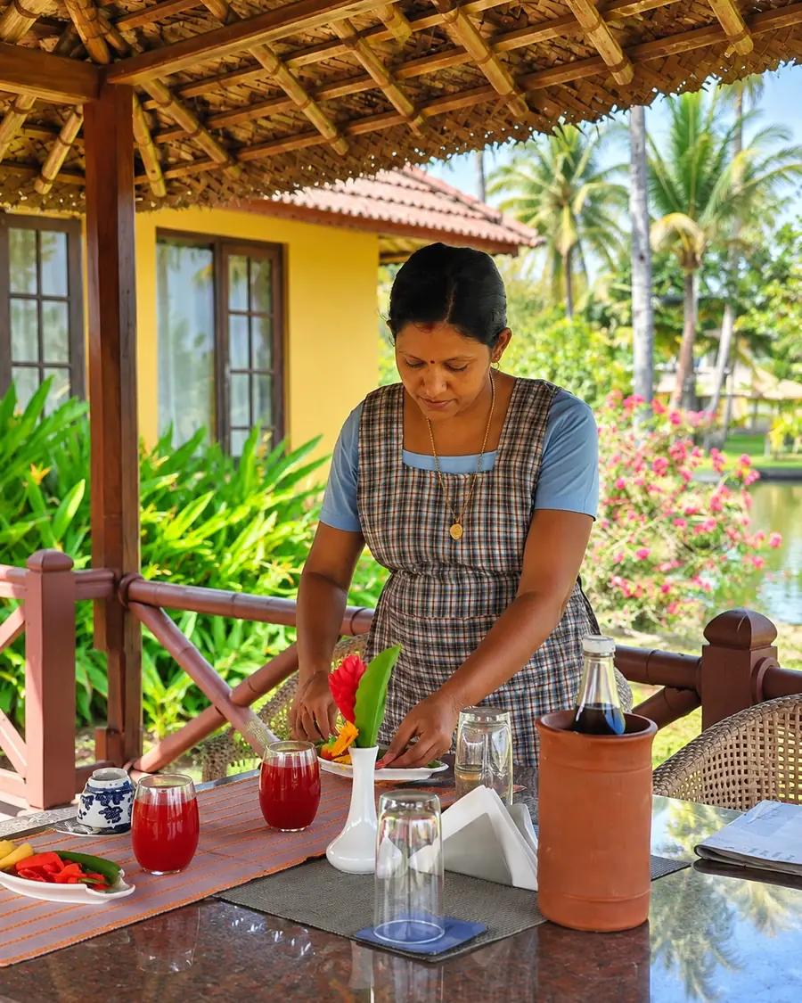 A member of the Ameya team setting a table with fresh juice and flowers on a pavilion by the lake