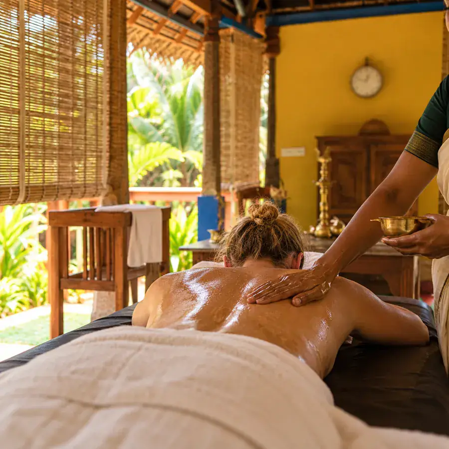 A guest receiving a warm oil Ayurvedic massage in the thatched spa