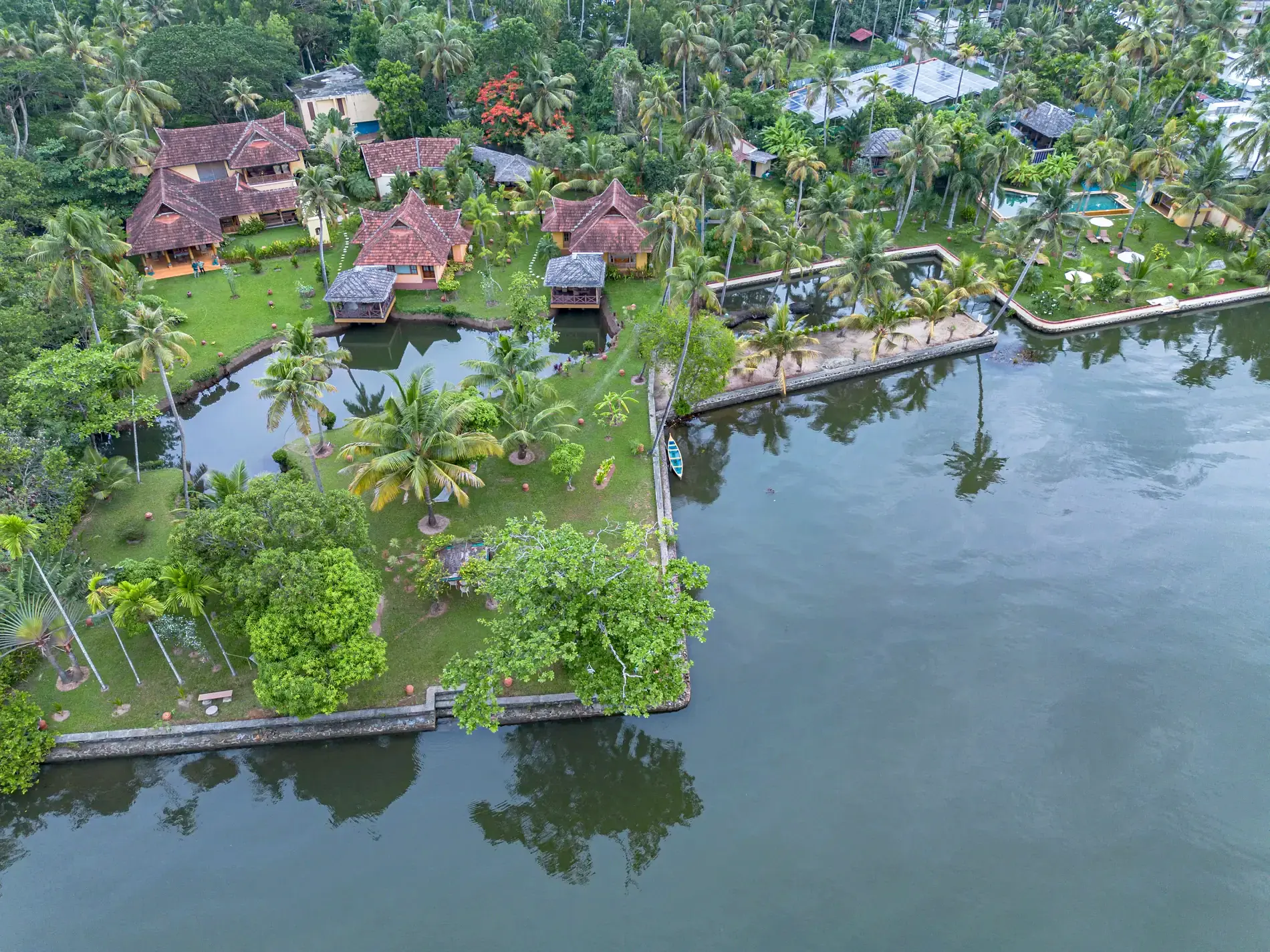 Aerial view of Ameya: tiled cottages and pavilions in a palm garden on the shore of Vembanad Lake