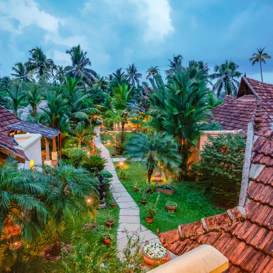 Dusk over tiled roofs and palms, garden lamps lit along the path