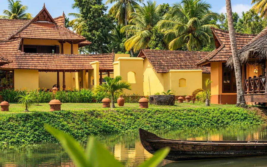 The main house in late sun: tiled roofs and yellow walls above the lawn, a wooden canoe moored in the canal